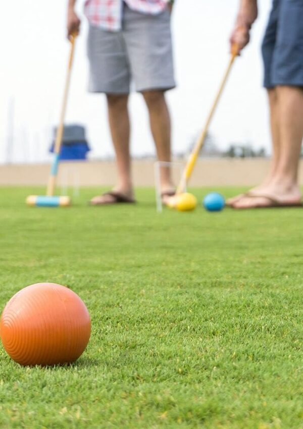 adults playing croquet on a green lawn