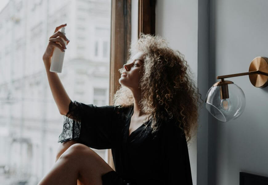 woman spraying fragrance on her hair