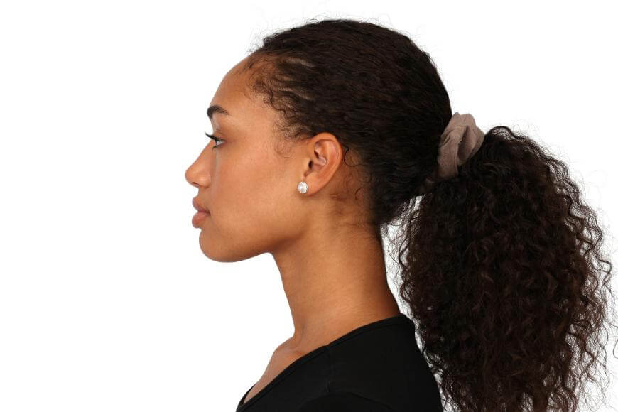 A young woman with curly hair tied back in a ponytail with a scrunchie, wearing a black top and stud earrings, is shown in profile view against a white background.