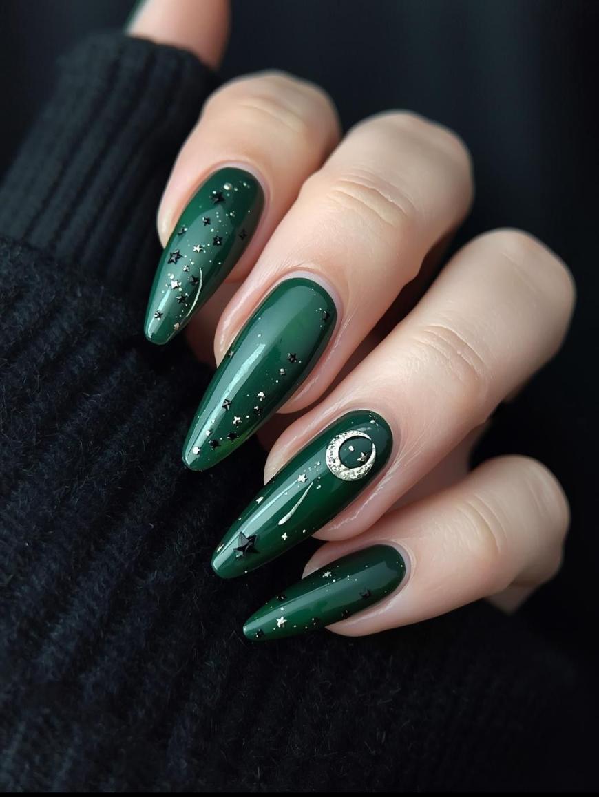 A hand with long, almond-shaped nails painted dark green, decorated with small silver stars and a crescent moon accent on the ring finger, resting against a black sweater.