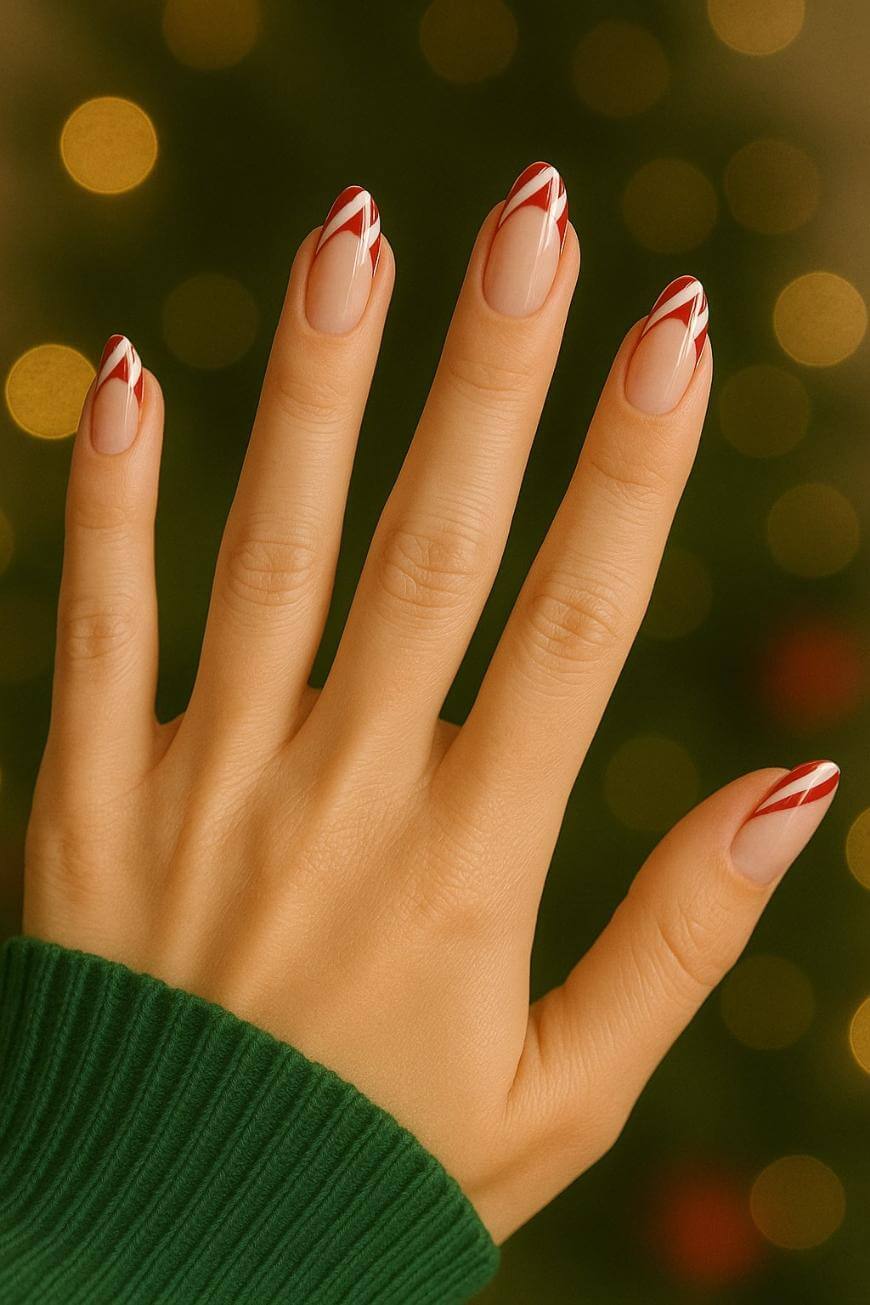 A hand with long, almond-shaped nails painted in a red and white striped candy cane design, set against a festive, golden bokeh background. The person is wearing a green sweater.