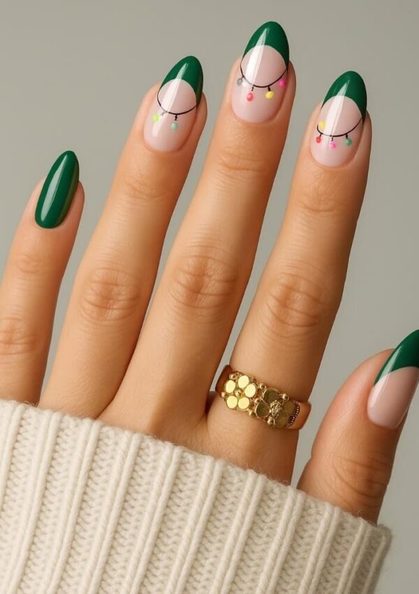 A hand with almond-shaped nails featuring green French tips, black curved lines, and colorful dot accents. The person wears a gold ring and a cream knit sweater.