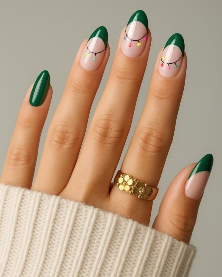 A hand with almond-shaped nails featuring green French tips, black curved lines, and colorful dot accents. The person wears a gold ring and a cream knit sweater.