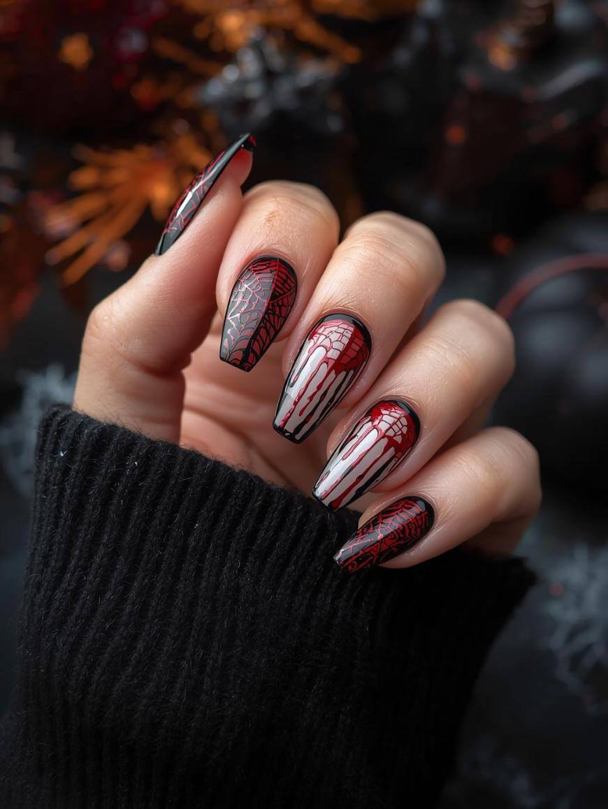 A hand with long, almond-shaped nails featuring Halloween-themed nail art: black and red spider webs and dripping white designs. The person is wearing a black sweater, and the background is blurred and dark.