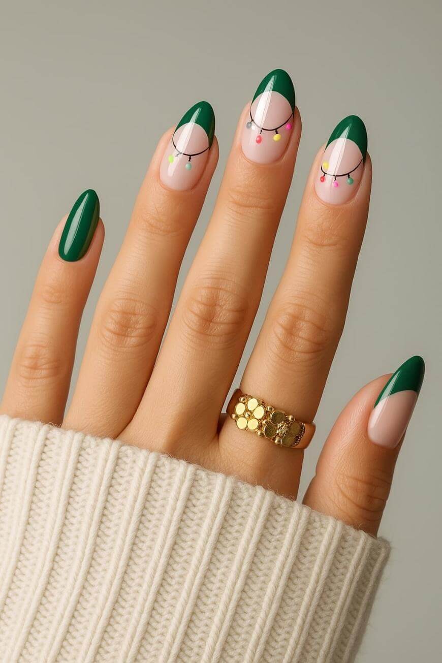 A hand with almond-shaped nails features green French tips and delicate string light designs. The person wears a textured gold ring and a cream-colored ribbed sweater.