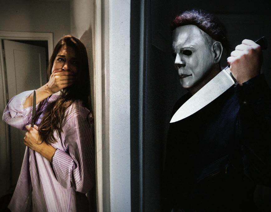 A frightened woman in pajamas covers her mouth in fear while a person in a white mask and dark clothes holds a large knife, lurking menacingly around a corner.