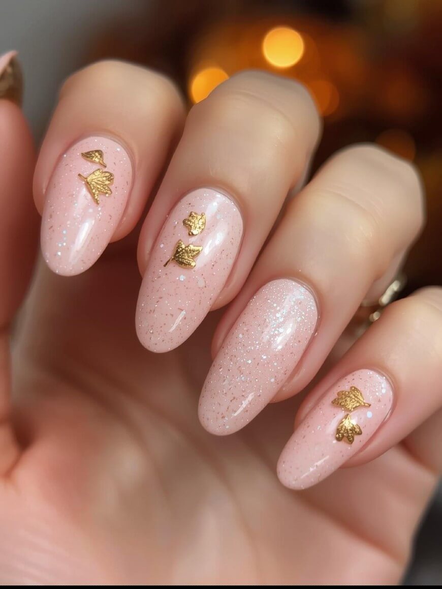 A hand with almond-shaped nails painted in light pink polish with subtle glitter, each nail decorated with small gold metallic butterfly accents.