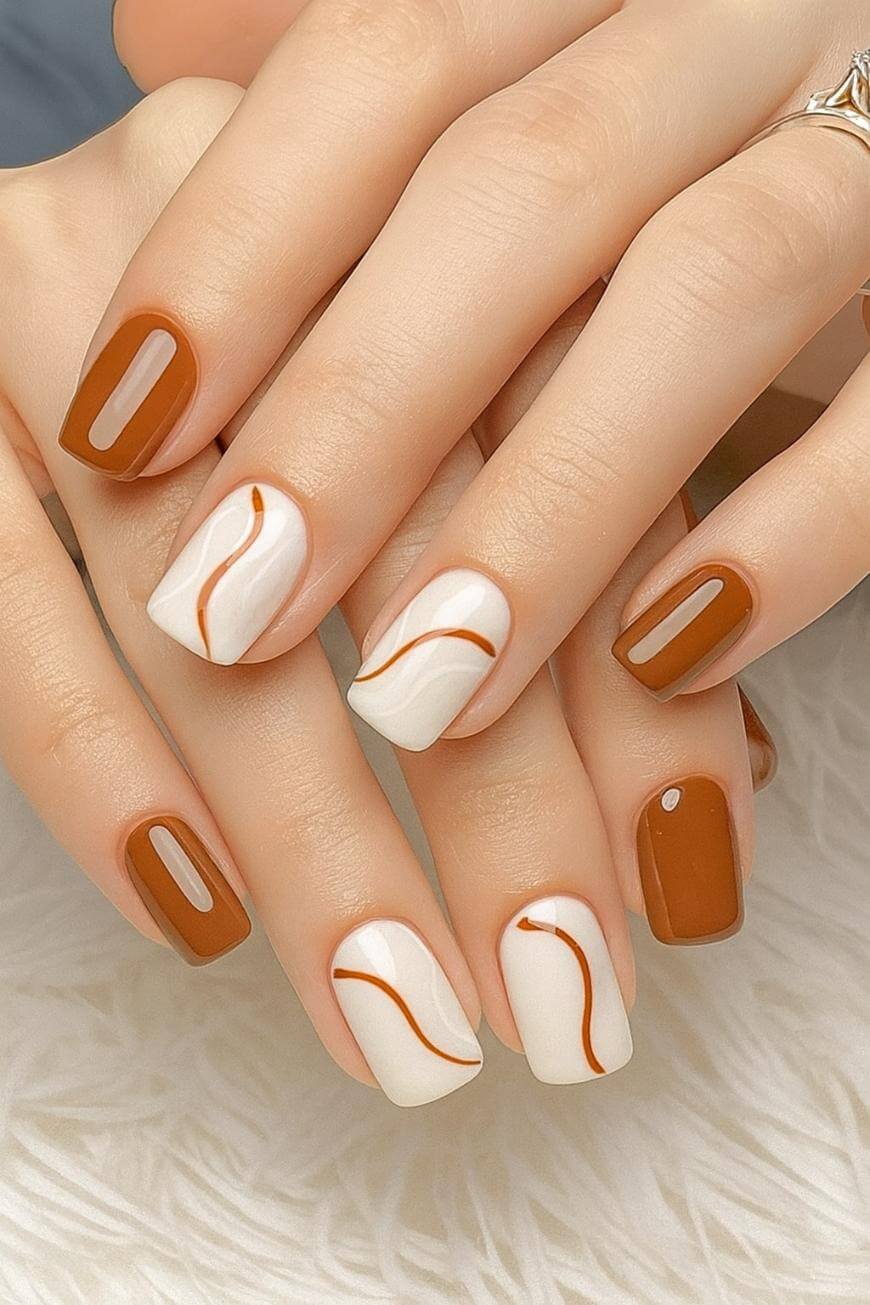 A hand with square-shaped nails features a manicure with alternating brown and white nail polish. The white nails have curved brown lines as minimalist designs. The nails are neatly styled and glossy.