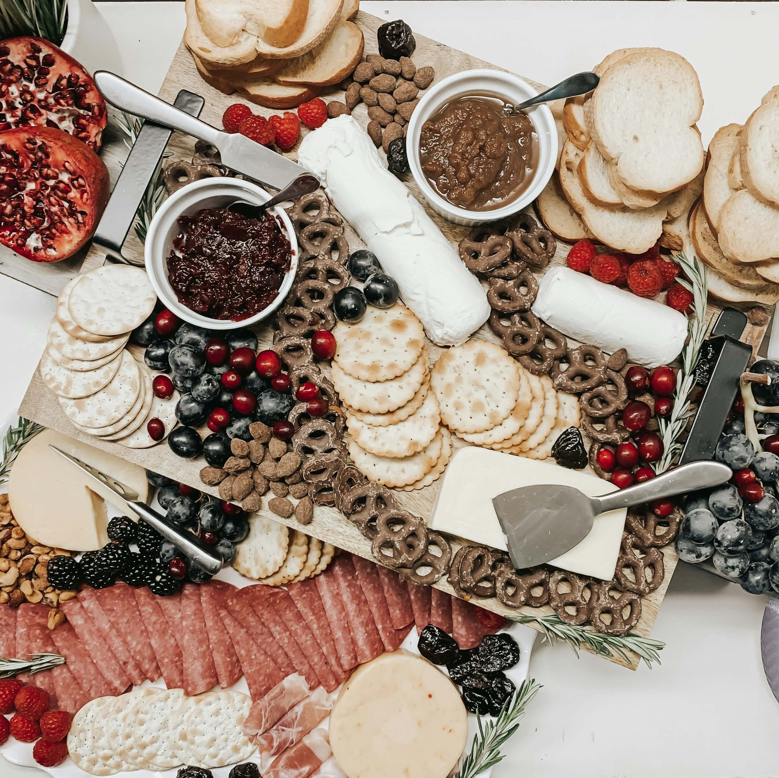 A charcuterie board with assorted crackers, cheeses, sliced meats, pretzels, spreads, berries, nuts, and sliced bread, arranged with festive garnishes and serving utensils.