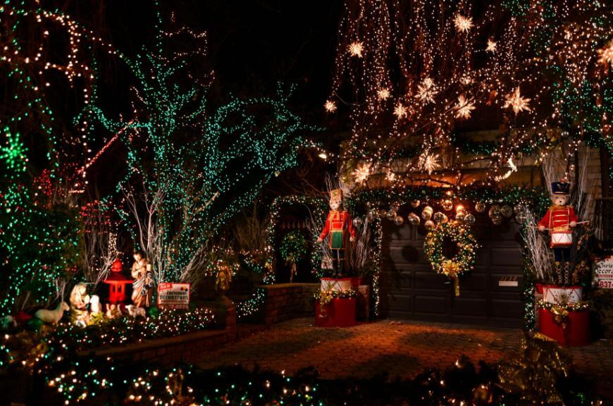 A house decorated for Christmas with colorful lights, wreaths, star-shaped ornaments, toy soldier statues, and festive figures, creating a bright and cheerful holiday display at night.