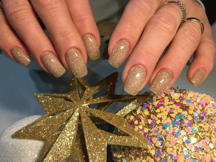 Hands with gold glittery nail polish are shown holding a gold glitter star ornament and a ball covered in multicolored sequins, suggesting a festive or holiday theme.