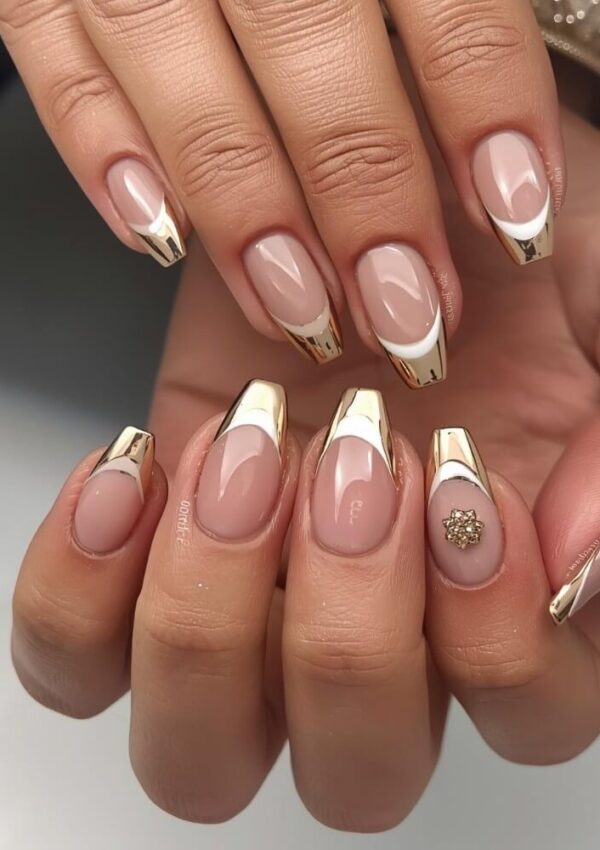 Hands with almond-shaped nails featuring a nude base and shiny gold French tips; one nail is decorated with a small gold embellishment. The nails have a glossy finish and elegant, modern design.