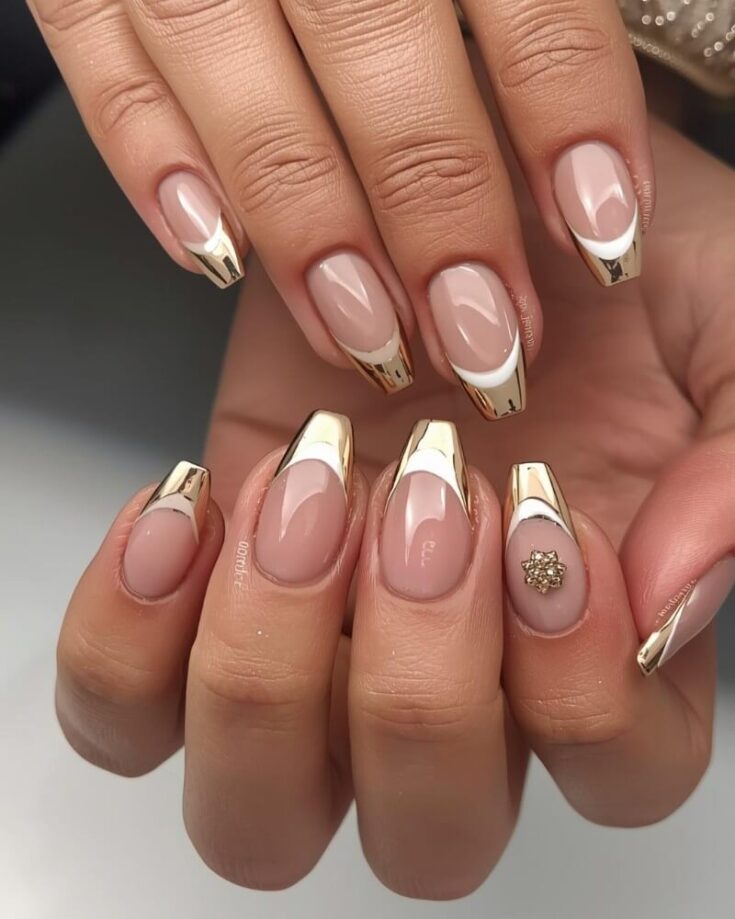 Hands with almond-shaped nails featuring a nude base and shiny gold French tips; one nail is decorated with a small gold embellishment. The nails have a glossy finish and elegant, modern design.