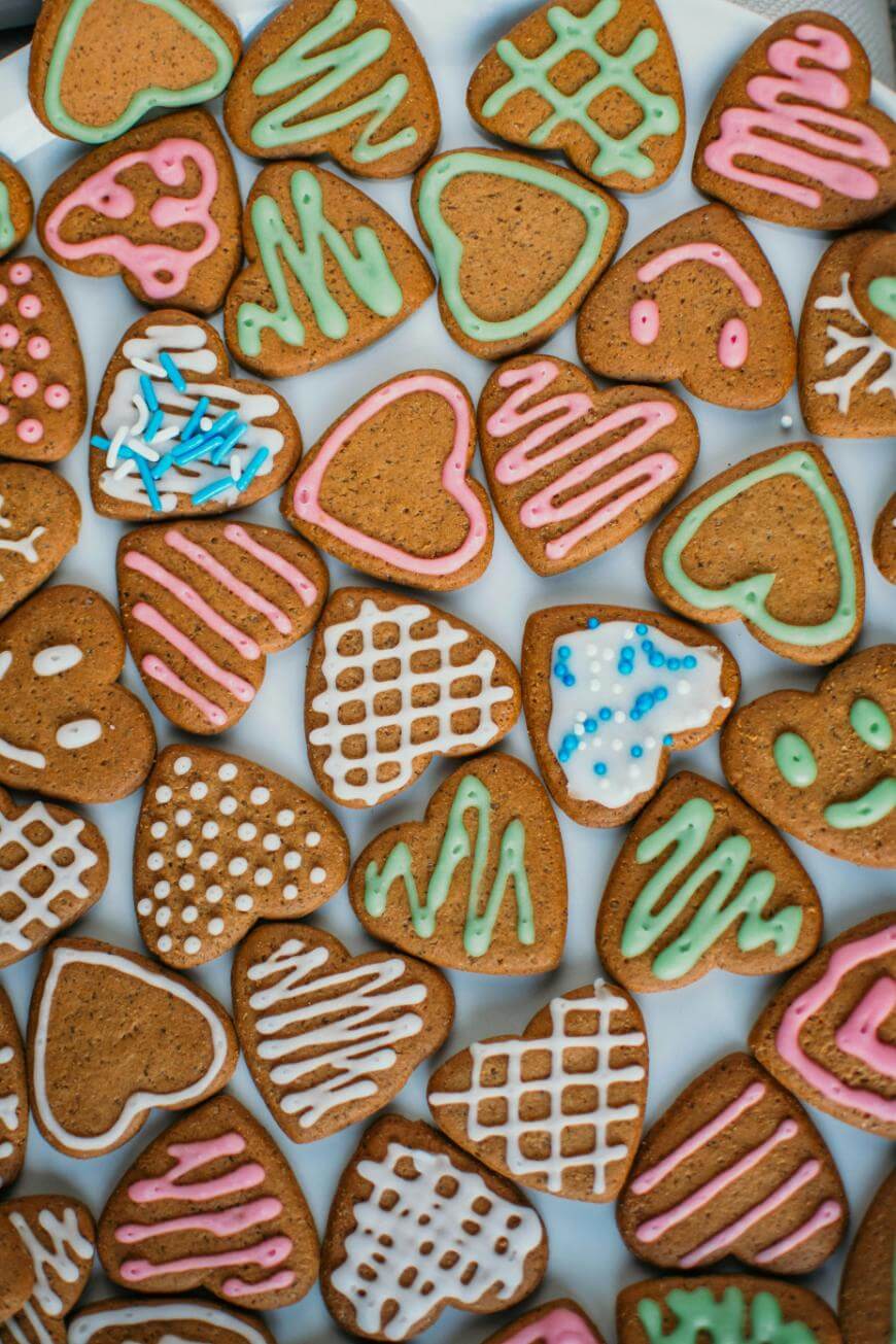 Heart-shaped cookies decorated with colorful pastel icing in various patterns, such as stripes, dots, and zigzags, arranged closely together on a white surface.
