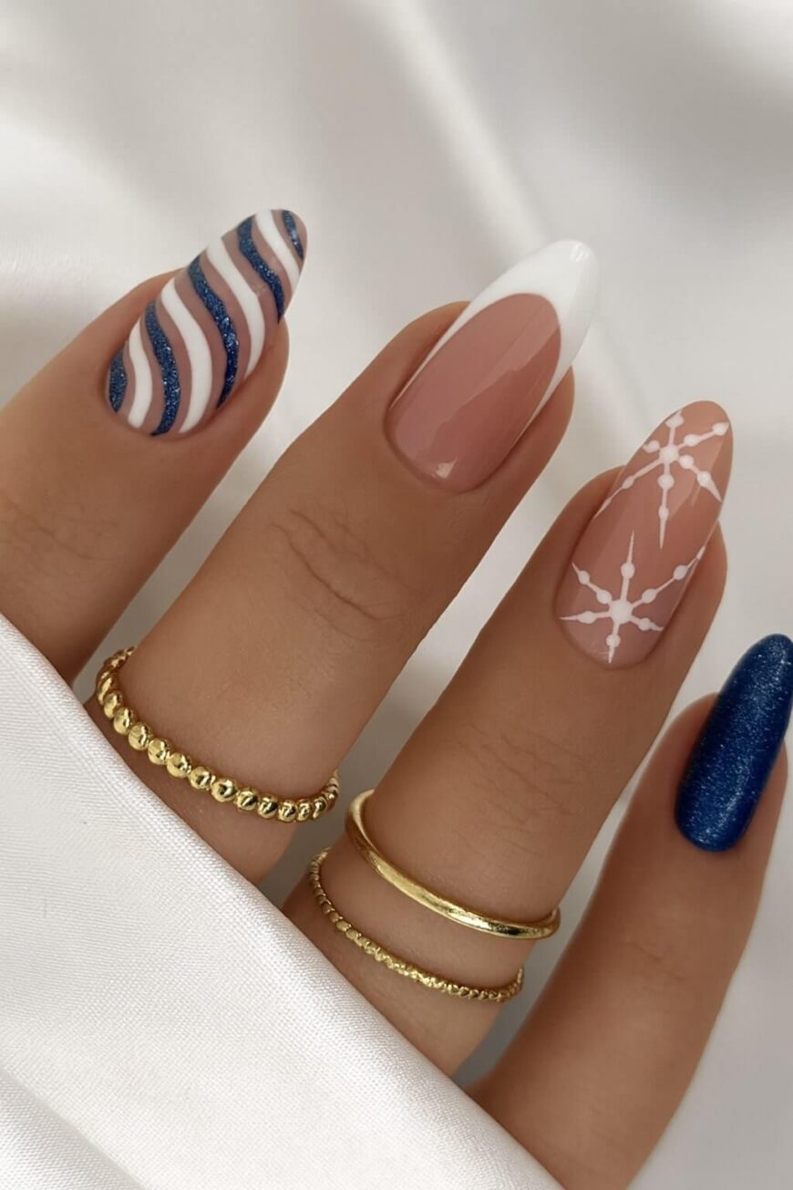 A hand with manicured nails featuring different designs: blue and white wavy stripes, a French tip, a sheer pink with white lines, and solid blue glitter; gold rings adorn the fingers.