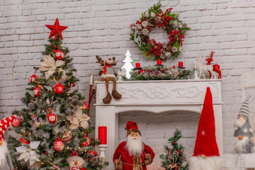 A festive Christmas scene with a decorated tree, a white mantel adorned with a wreath, candles, and ornaments, and various holiday figures including Santa Claus, reindeer, and gnomes.