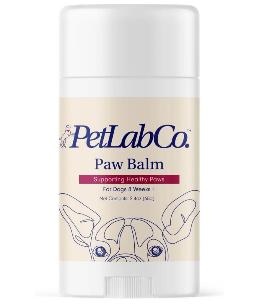 A container of PetLab Co. Paw Balm for dogs 8 weeks and older, featuring a drawing of a dogs face and product details on the label. The stick contains 2.4 oz (68g) and supports healthy paws.