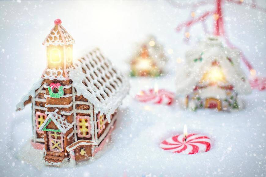 A gingerbread house decorated with icing and candy sits in snowy surroundings, glowing warmly. In the background are more gingerbread houses and peppermint candies, creating a festive and magical winter scene.