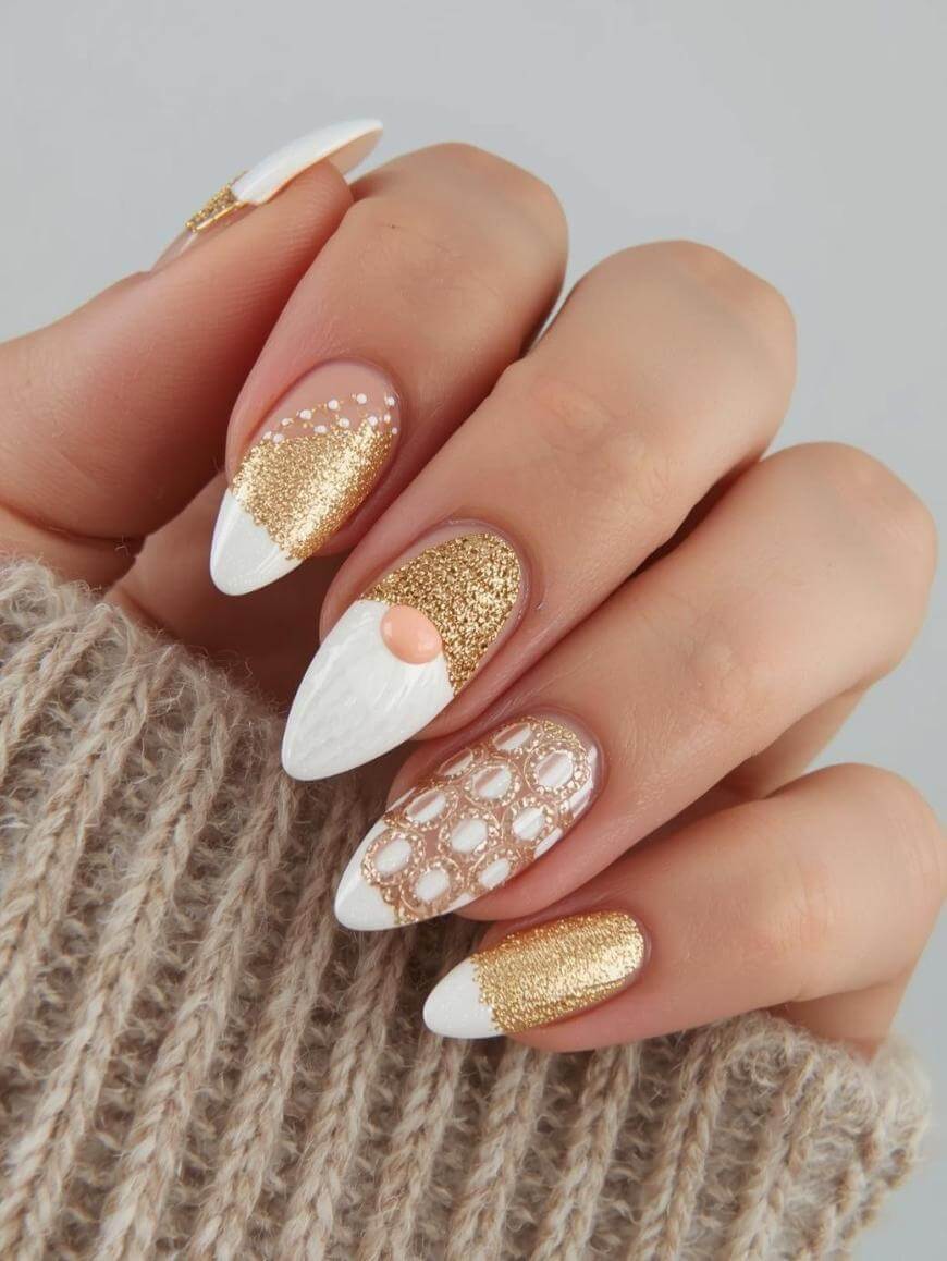 A hand with almond-shaped nails featuring gold glitter, white tips, geometric patterns, and a textured peach accent, shown against a beige knitted sleeve.