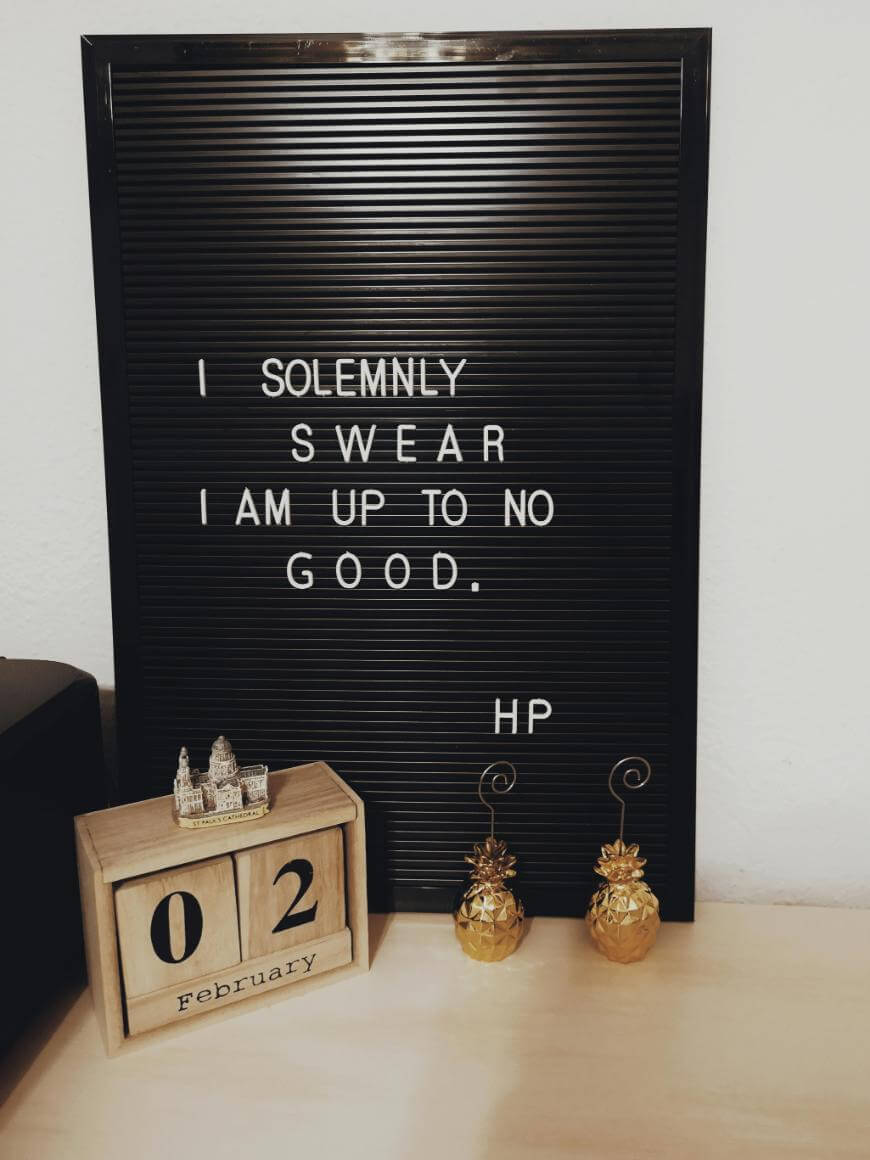A black letter board displays the quote, I solemnly swear I am up to no good. HP. In front, a wooden block calendar shows February 2nd, and two small golden pineapple ornaments are on the right.