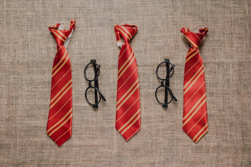 Three red and yellow striped neckties and three round black glasses are neatly arranged alternately on a burlap fabric background.
