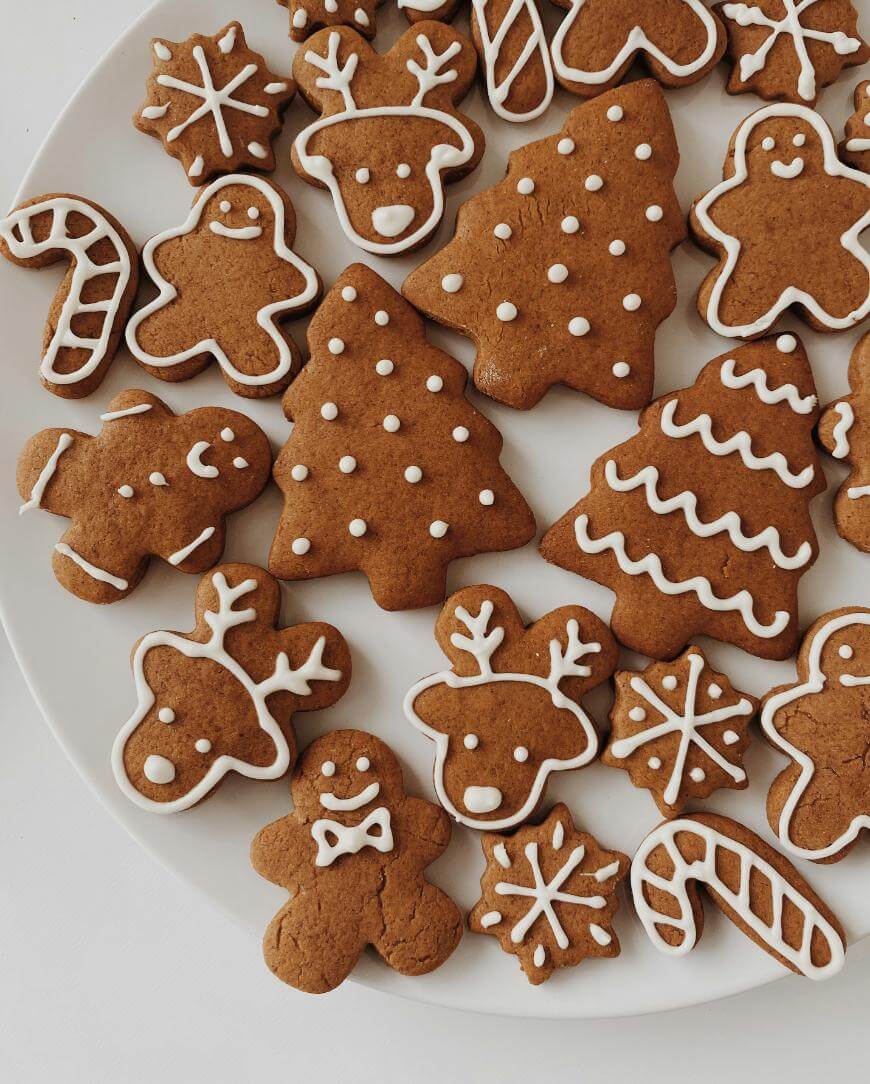 A plate of decorated gingerbread cookies shaped like Christmas trees, reindeer, gingerbread people, snowflakes, and candy canes, all outlined with white icing.