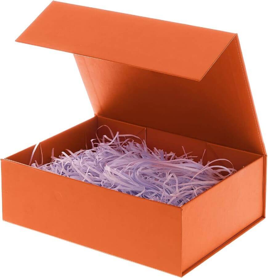 An open orange gift box filled with shredded light purple paper, with the lid propped up and the inside of the box empty aside from the paper.