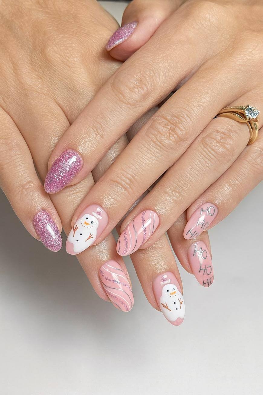 Hands with long, almond-shaped nails featuring pink glitter, pink and white swirl designs, snowman art, and “Ho Ho Ho” text, creating a festive holiday manicure.