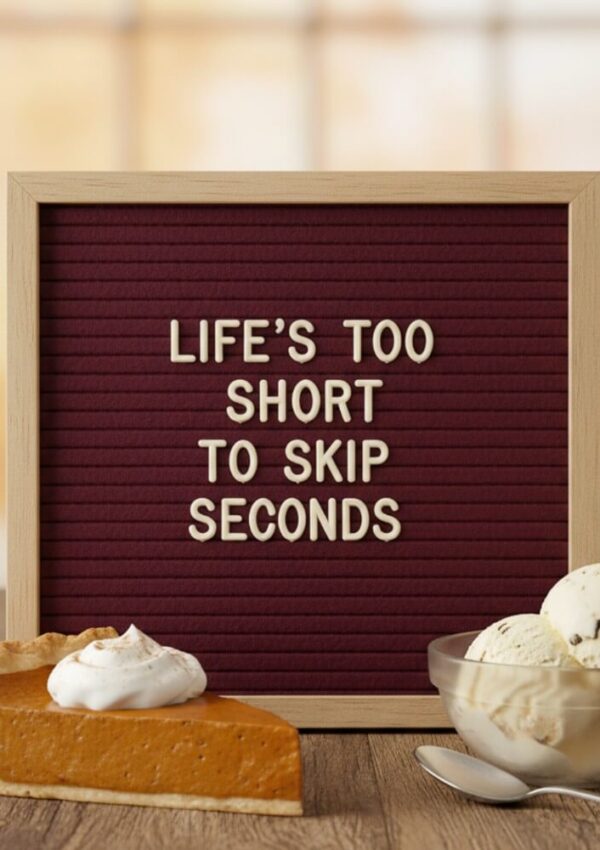 A sign with white letters on a maroon felt board reads Lifes too short to skip seconds. In front, there is a slice of pumpkin pie with whipped cream and a bowl of vanilla ice cream.