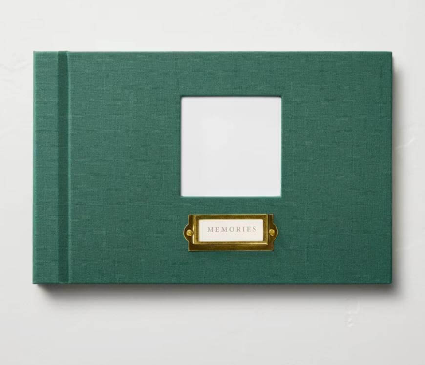 A green hardcover photo album with a blank square window in the center and a gold label holder below it that reads MEMORIES. The album is set against a white background.