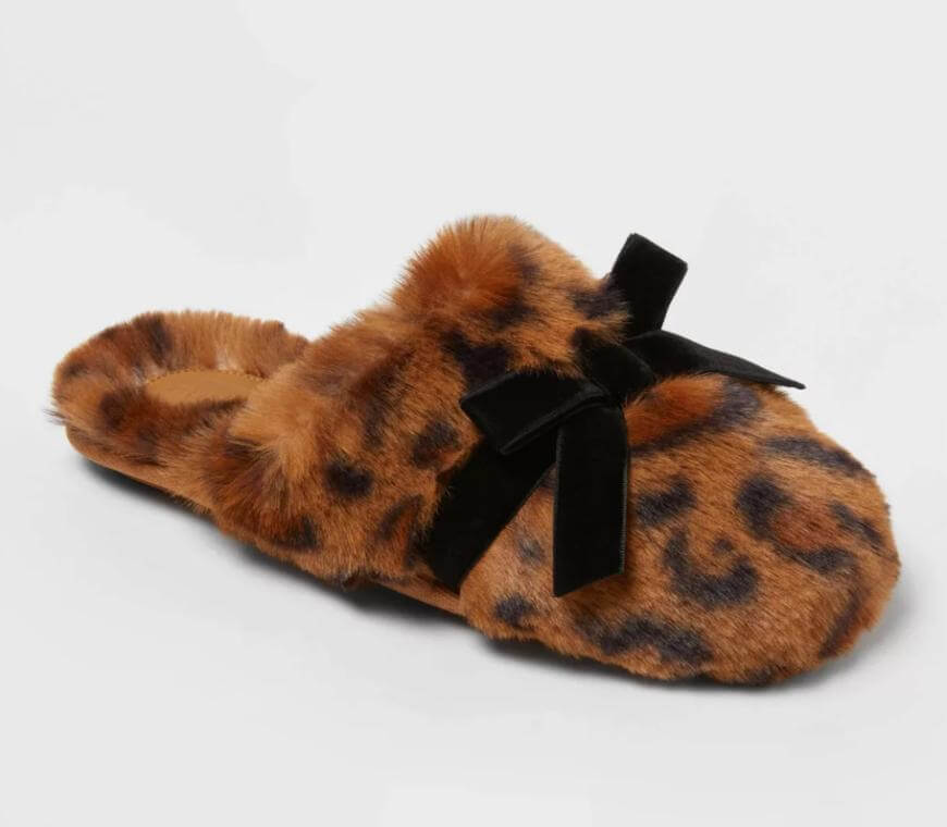 A fuzzy slipper with a brown and black leopard print pattern, featuring a black velvet bow on top.