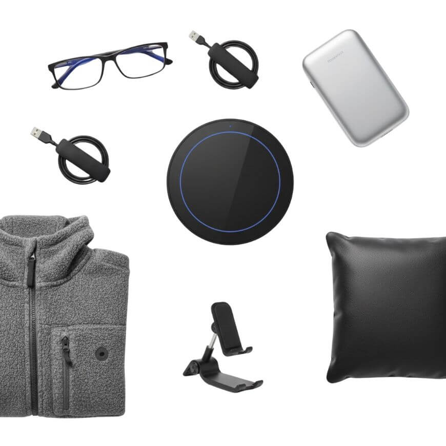A collection of office essentials including eyeglasses, two USB cables, a portable charger, a gray fleece jacket, a phone stand, a wireless charging pad, and a black pillow, all arranged on a white background.