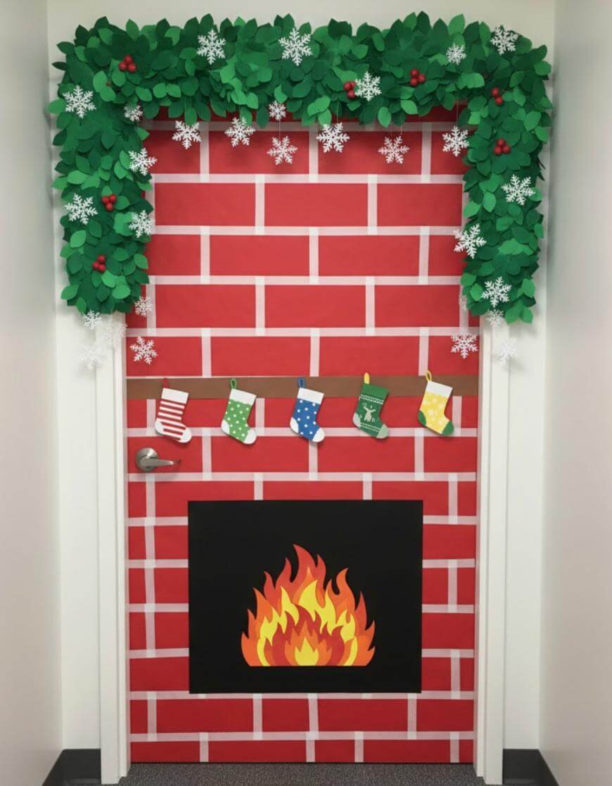 A door decorated as a brick fireplace with a paper fire, hanging stockings, paper snowflakes, and green paper garland with red berries along the top.