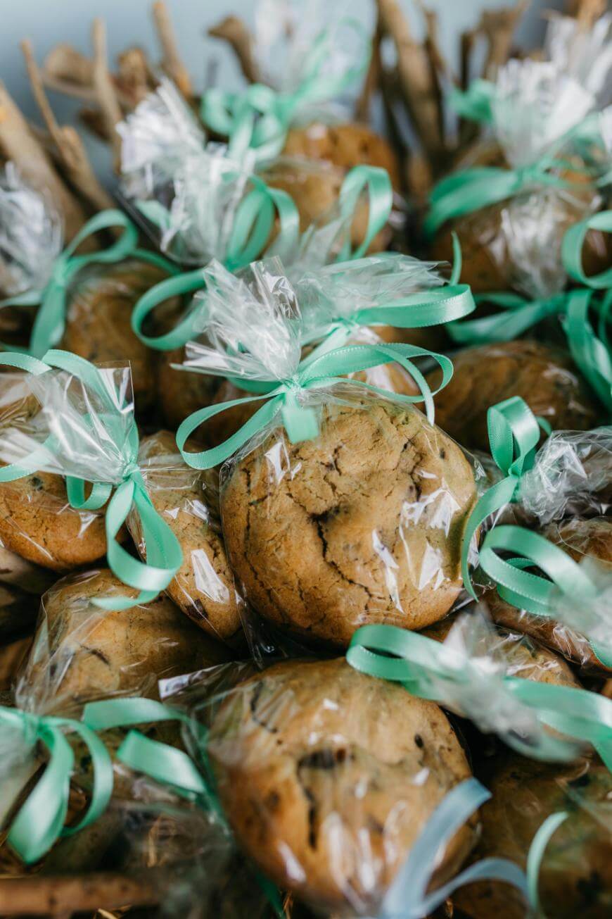 Stacks of chocolate chip cookies wrapped in clear plastic bags and tied with light green ribbons, arranged closely together for gift giving or an event.