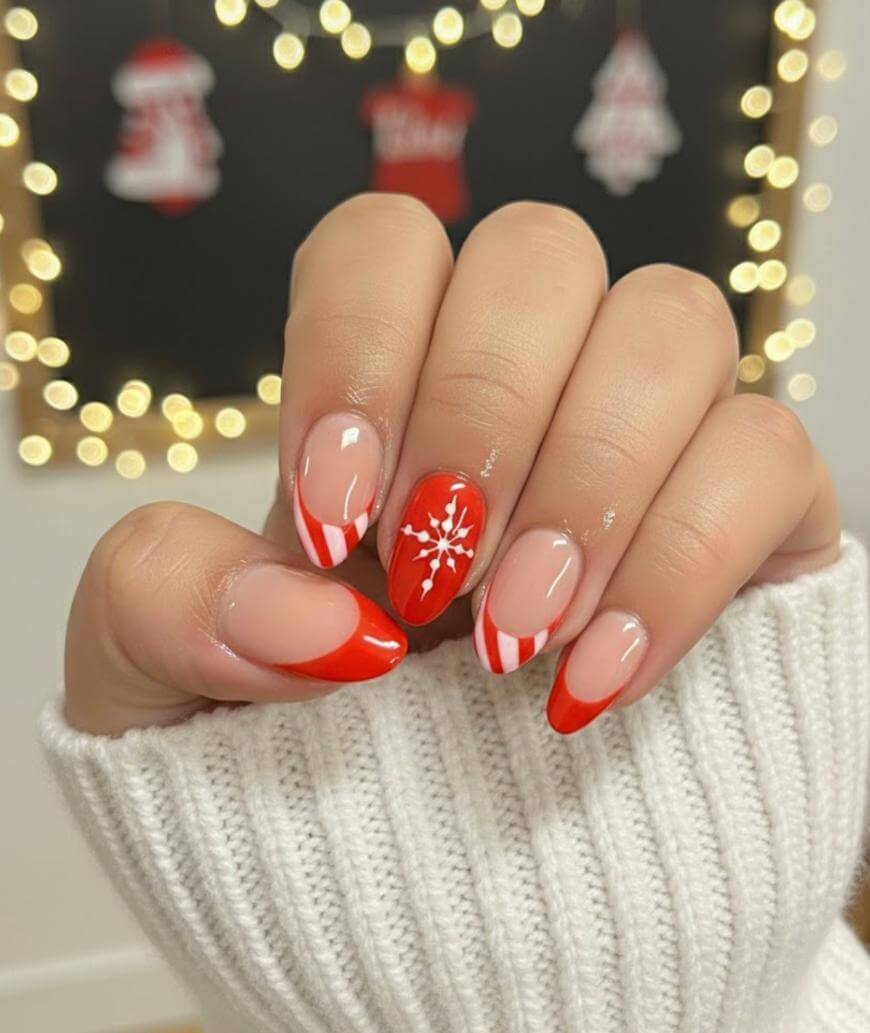 A hand with festive red and white Christmas-themed nail art, including candy cane stripes, solid red, and a snowflake design, is shown against a blurred background with fairy lights and holiday decorations.