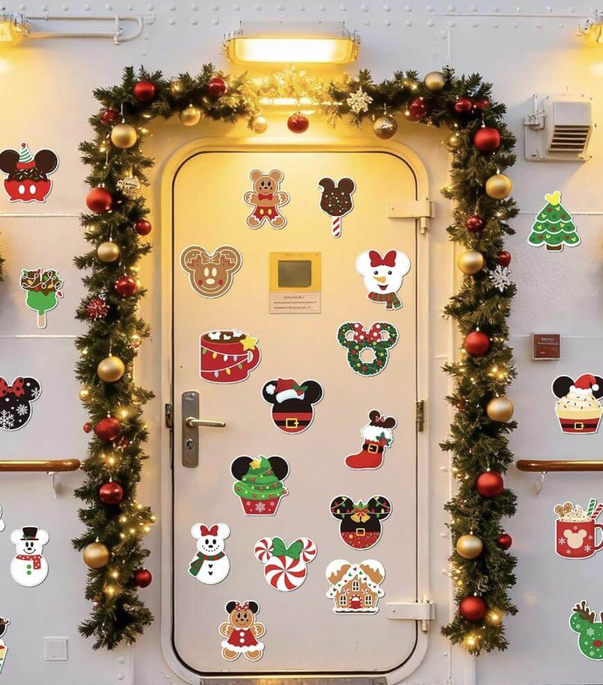 A white door decorated with festive holiday stickers featuring Mickey Mouse and Christmas-themed characters, surrounded by garlands with gold and red ornaments and twinkling lights.