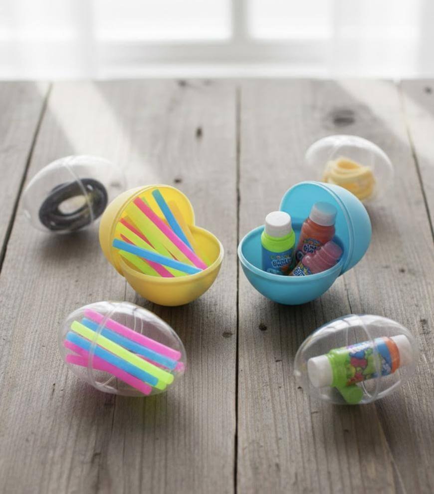 Several plastic eggs, some open and some closed, contain items like hair ties, colorful straws, bottles of bubbles, and small rolls of tape, arranged on a wooden surface in natural light.