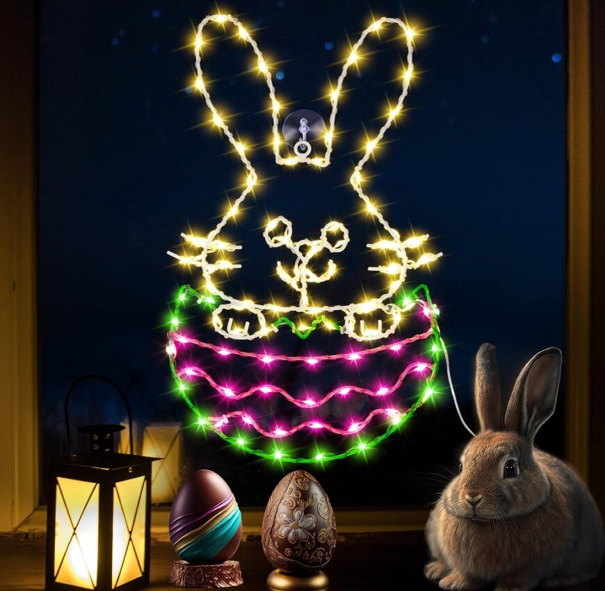 A window displays a glowing bunny outline made of string lights above a basket and Easter eggs. A lantern, three decorated eggs, and a brown rabbit sit on the windowsill, with a nighttime sky visible outside.