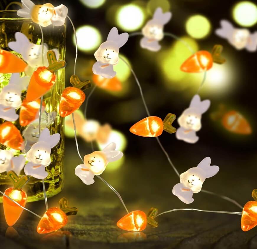 String lights featuring glowing bunny faces and orange carrots are draped around a glass jar, with a blurred green and yellow background creating a festive, cozy atmosphere.