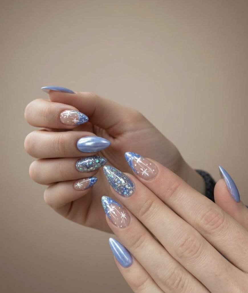 A hand with long, almond-shaped nails decorated with a mix of glossy light blue polish, blue glitter, and white snowflake designs on a neutral background.