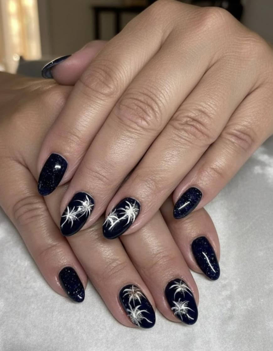 A close-up of hands with dark blue, glossy nails featuring white palm tree designs on several nails, resting on a light surface. The nails are well-manicured and artfully decorated.