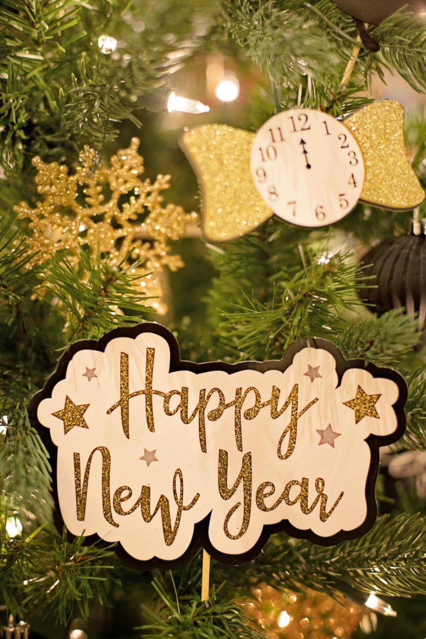 A festive Christmas tree decorated with a gold snowflake, a clock ornament, and a sign that says Happy New Year in glittery gold letters among twinkling lights and green branches.