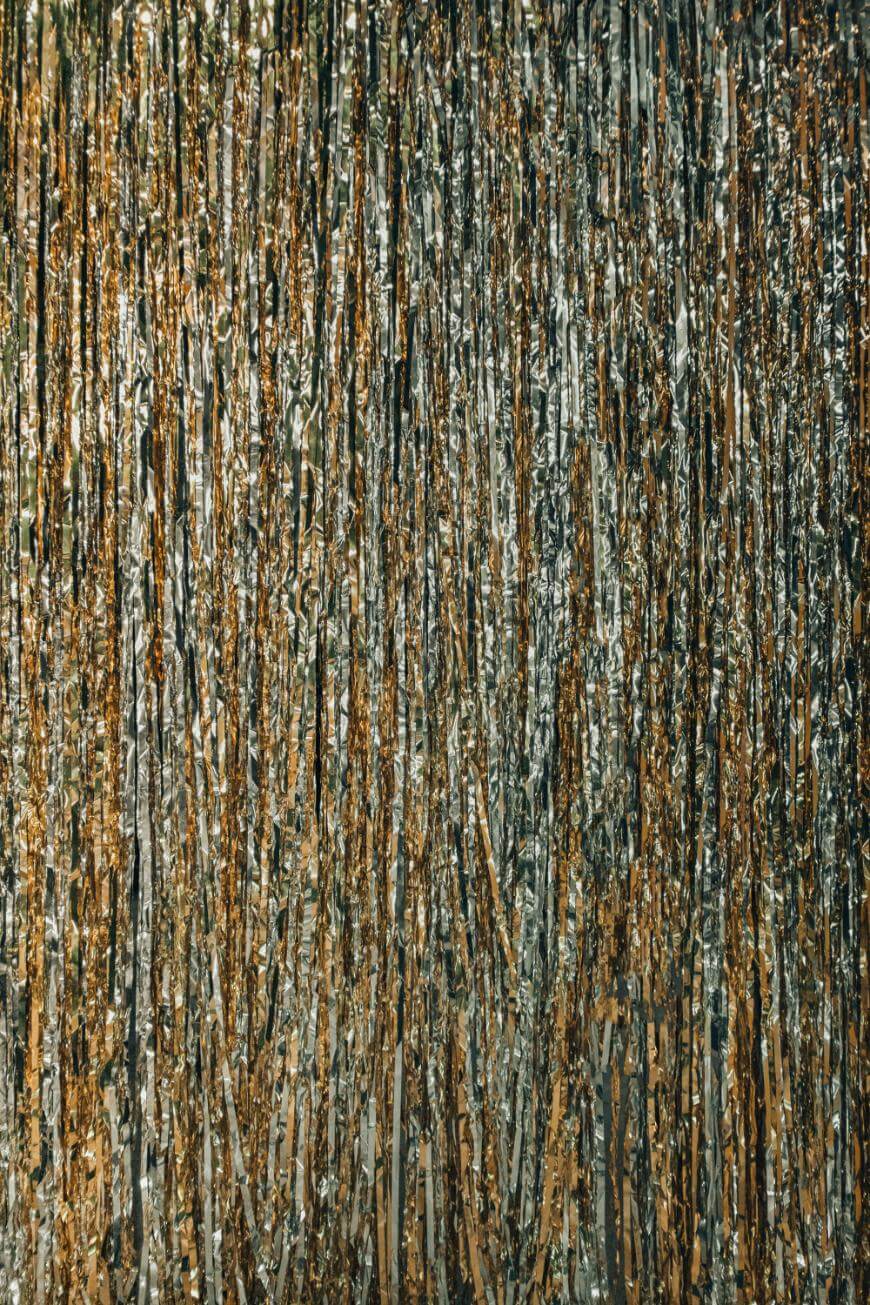 A dense curtain of metallic gold and silver tinsel strands hangs vertically, creating a shimmering, festive backdrop with a sparkling, reflective surface.