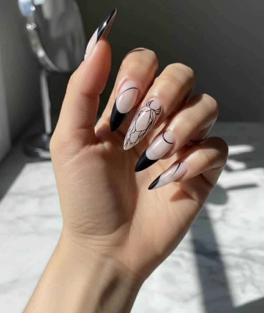 A hand with long almond-shaped nails featuring black tips and minimalist black line art designs, including abstract shapes and a flower outline, shown in natural lighting.