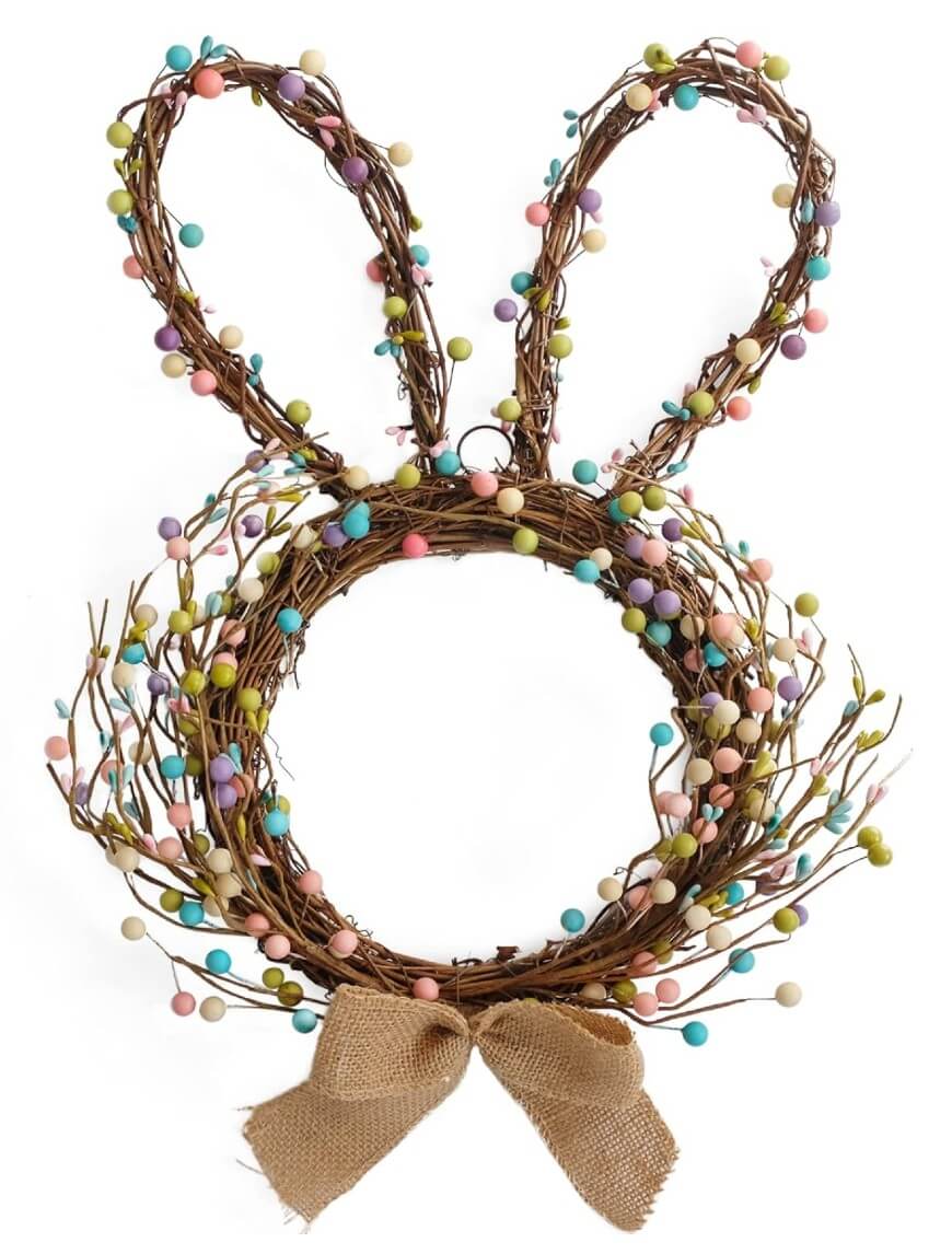 A wreath made of twigs and decorated with pastel-colored beads is shaped like a bunnys head with ears. A brown burlap bow is attached at the bottom.