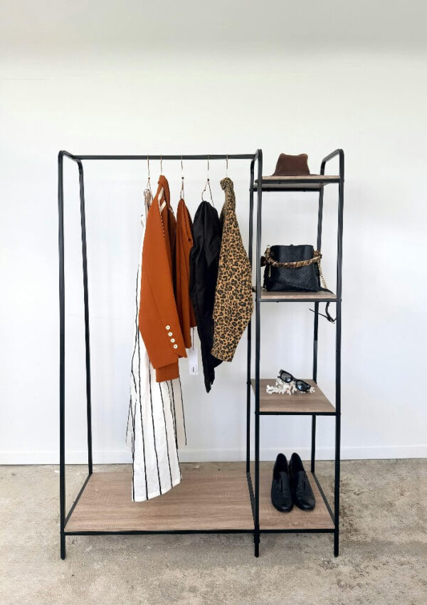 A minimalist black metal clothing rack with a wooden shelf, holding a striped dress, rust blazer, black jacket, leopard-print coat, black shoes, a black handbag, brown hat, and some small accessories.