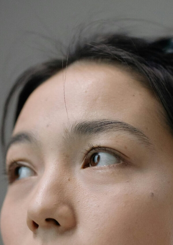 A close-up of a persons face focusing on the eyes and forehead. The individual is looking to the side, and a single strand of hair falls across their forehead. The background is neutral and out of focus.