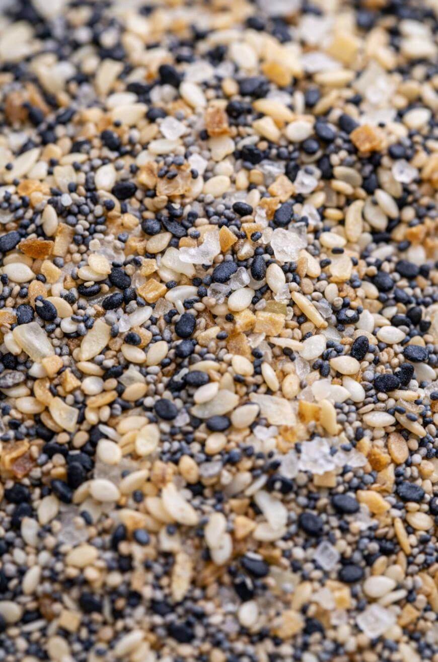 A close-up view of a mixture of black and white sesame seeds, poppy seeds, dried garlic, dried onion, and coarse salt, resembling an everything bagel seasoning blend.