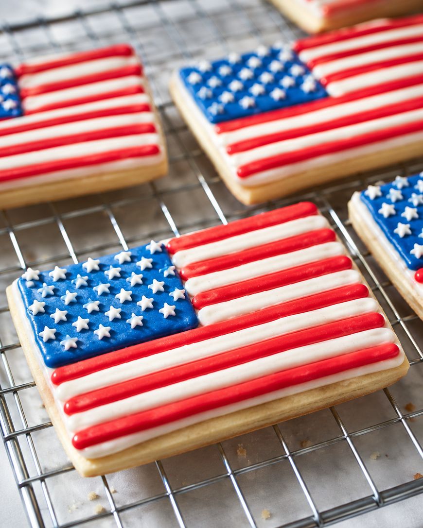 Rectangular sugar cookies decorated with icing to resemble the American flag, featuring red and white stripes and a blue corner with white stars, placed on a metal cooling rack.