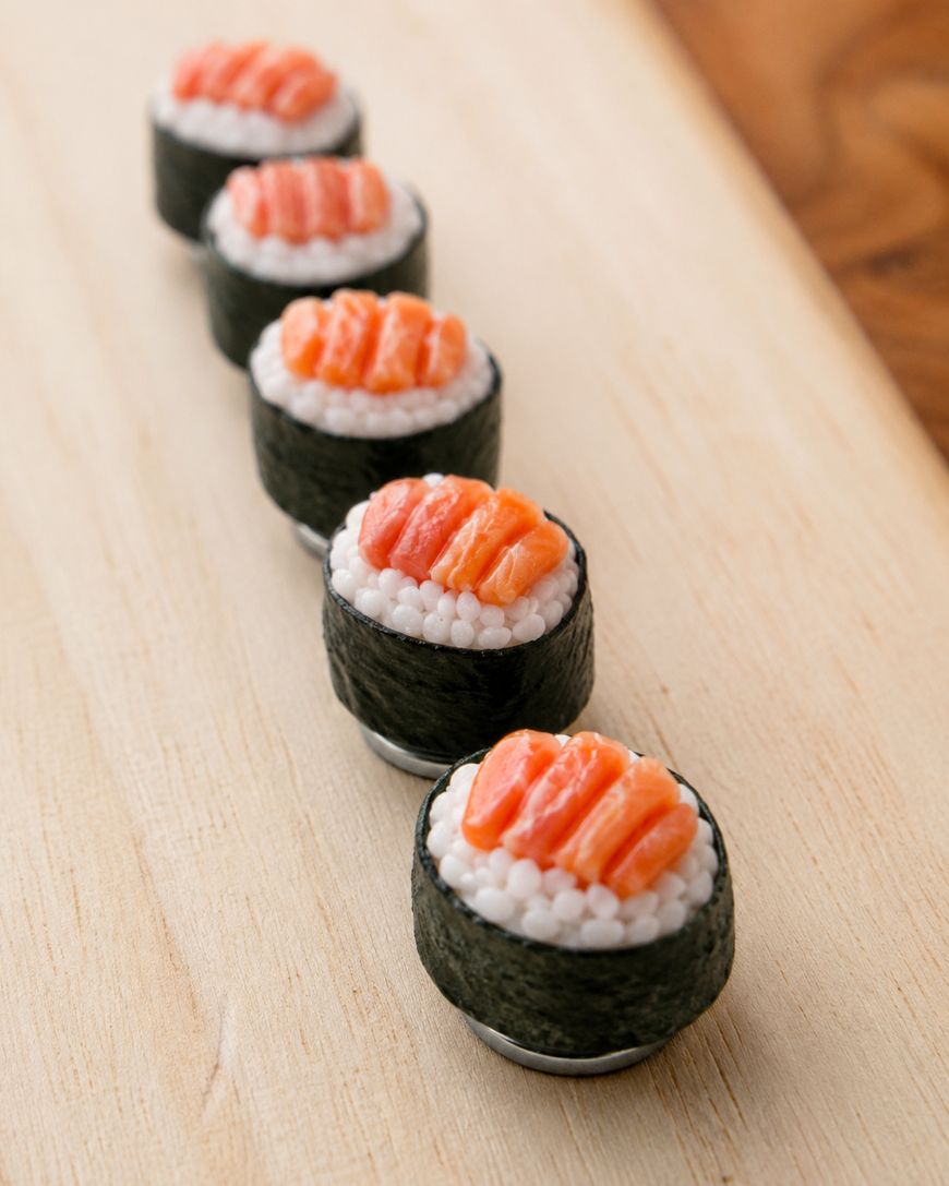 Five pieces of sushi with salmon and rice wrapped in seaweed are arranged in a neat row on a light wooden surface.